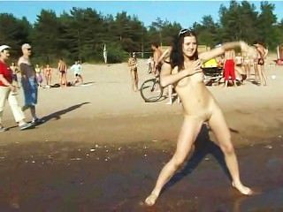 Adolescente delgado con los tetas alegres desnudos en una playa nudista